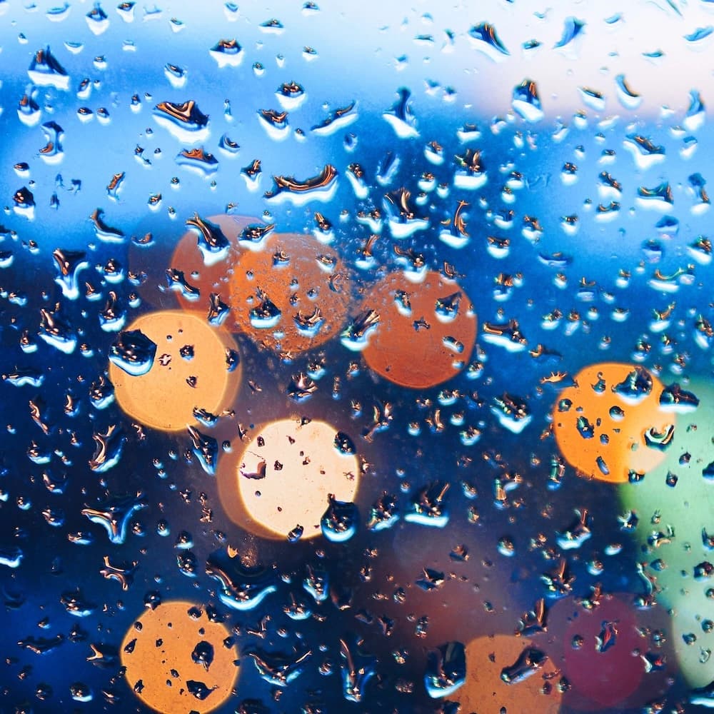Raindrops on a window with blurred city lights create a vibrant bokeh effect at night.